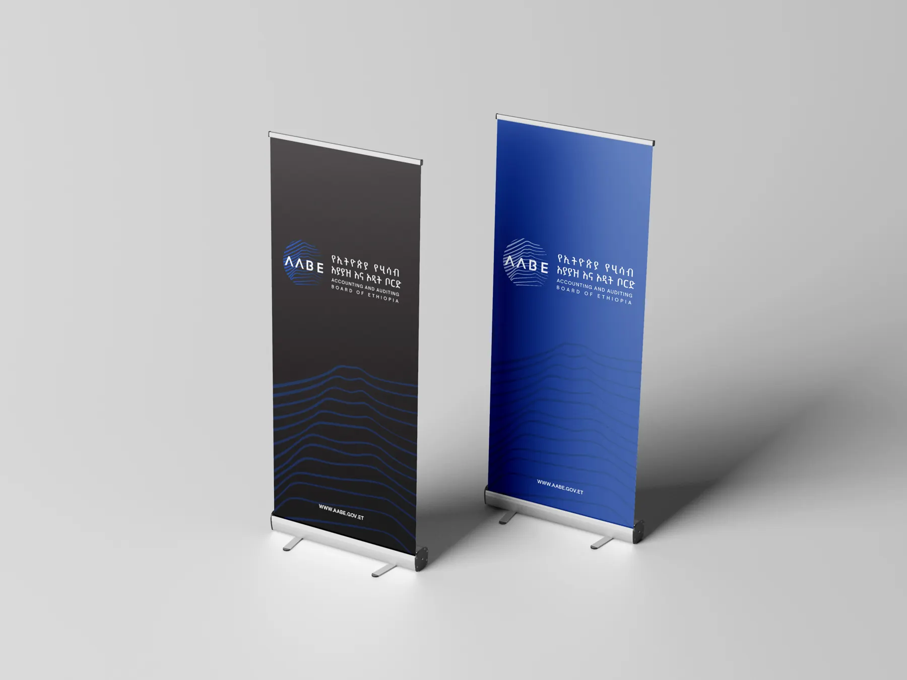 Two AABE roll-up banners standing side by side, one black and one blue, each with the bilingual logo and the line pattern.