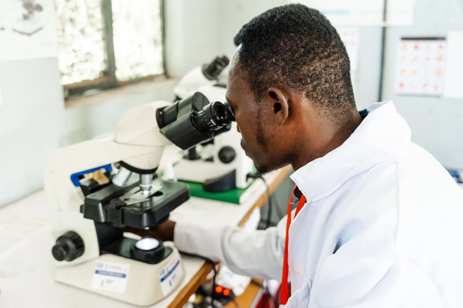 A laboratory technician in a white coat looks into a microscope.