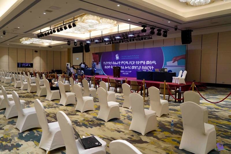 A hotel ballroom set for a NEBE event: rows of white chairs facing a stage with a large purple NEBE backdrop.
