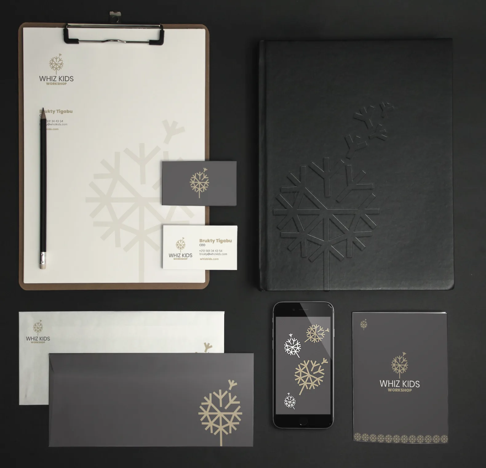 Whiz Kids stationery on a dark surface: letterhead on a clipboard, grey and white business cards, an embossed black notebook, envelopes, a phone screen and a folder, all carrying the dandelion.